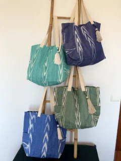 Cuatro bolsas artesanales de telas de lenguas mallorquinas en tonos azul, verde y turquesa sobre una escalera de madera