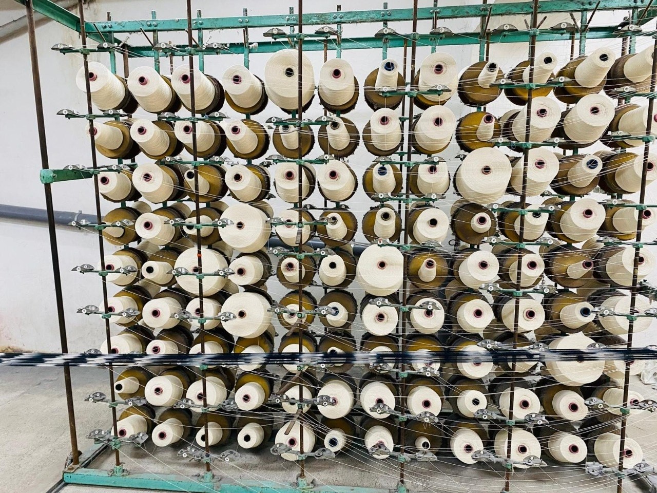 Bobinas de hilo claro dispuestas en una estructura metálica de un taller textil