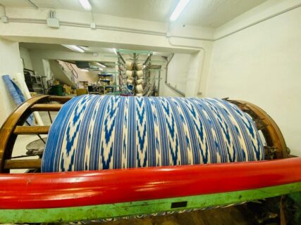 Hilos azules y blancos con dibujo de lenguas sobre un gran rodillo de madera en el taller