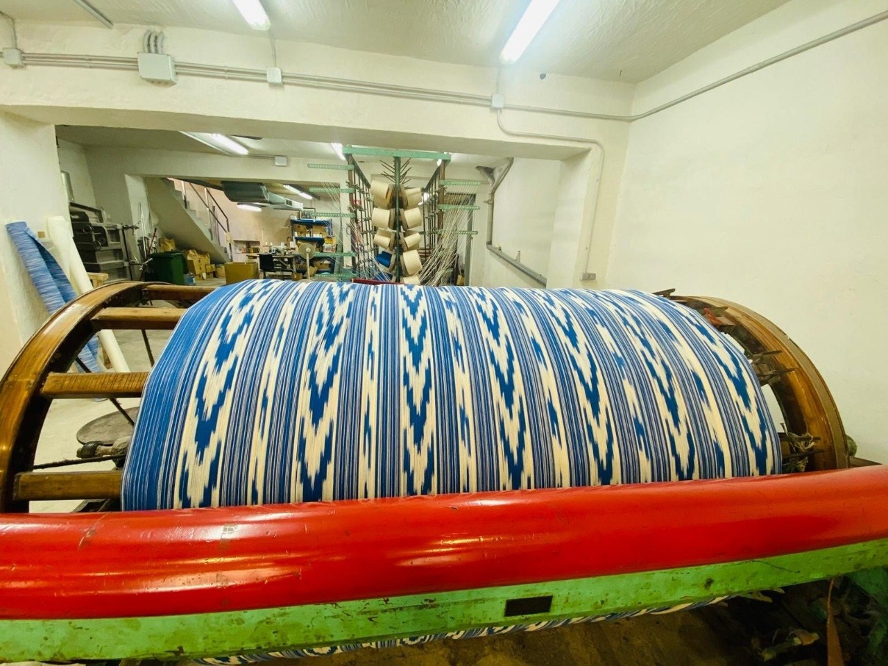 Hilos azules y blancos con dibujo de lenguas sobre un gran rodillo de madera en el taller